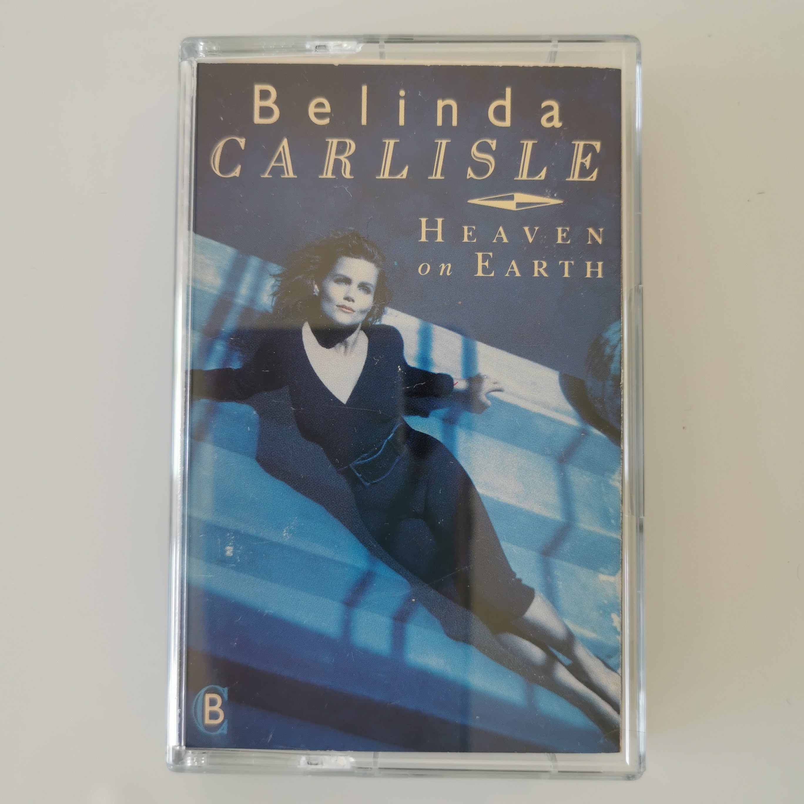 A cassette tape of Belinda Carlisle's album 'Heaven on Earth' in a clear plastic case, photographed against a plain off-white background.