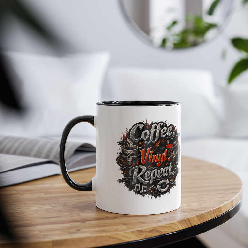 A white ceramic coffee mug with a black handle and interior, featuring a circular graphic that reads 'Coffee Vinyl Repeat' in stylized lettering with skulls and vinyl records. The mug is placed on a round wooden table in a softly blurred living room setting.