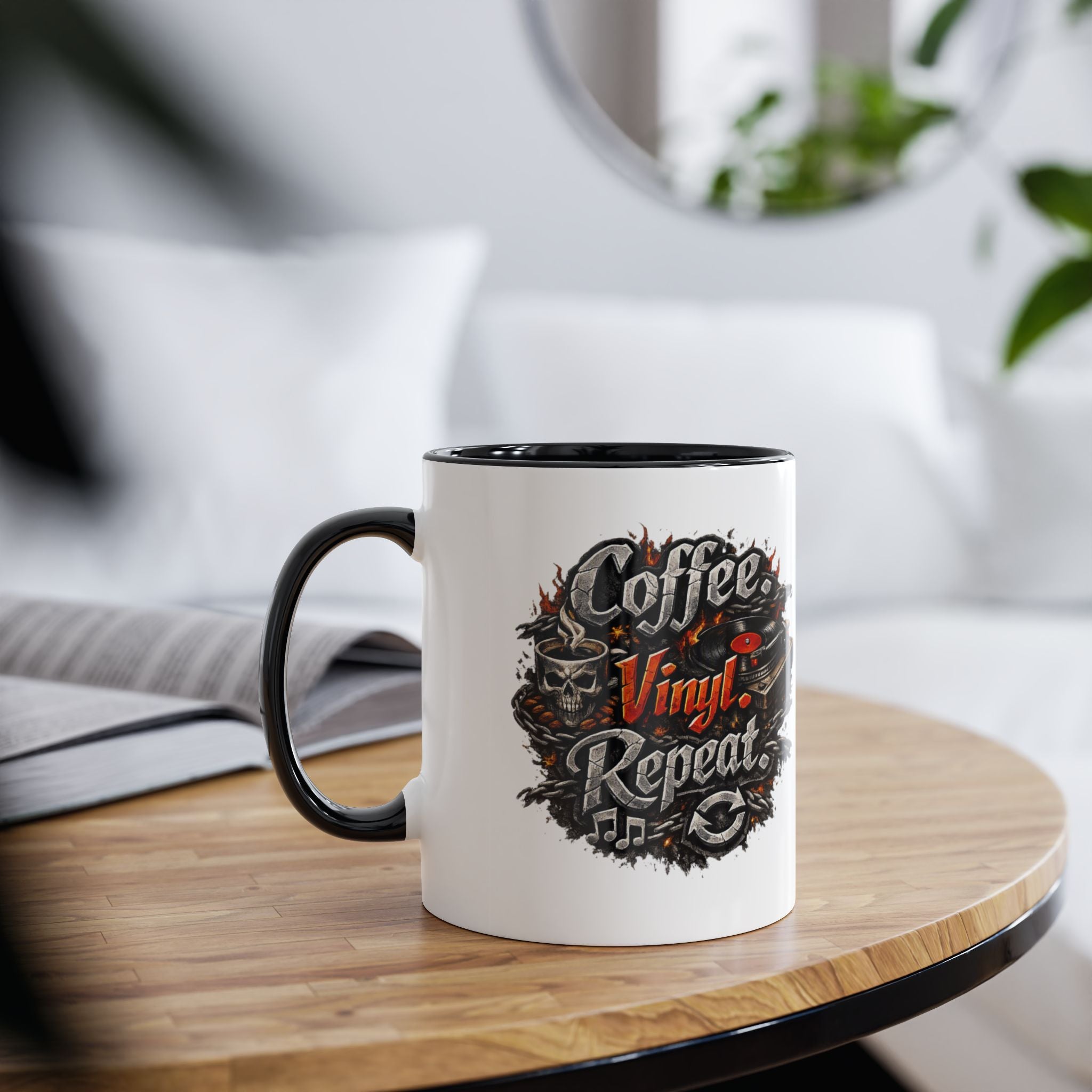 A white ceramic coffee mug with a black handle and interior, featuring a circular graphic that reads 'Coffee Vinyl Repeat' in stylized lettering with skulls and vinyl records. The mug is placed on a round wooden table in a softly blurred living room setting.