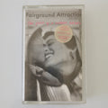 A cassette tape of Fairground Attraction's 'The first of a million kisses' with a black and white photo of a smiling woman on the cover, featuring a pink handwritten title and a gold sticker.
