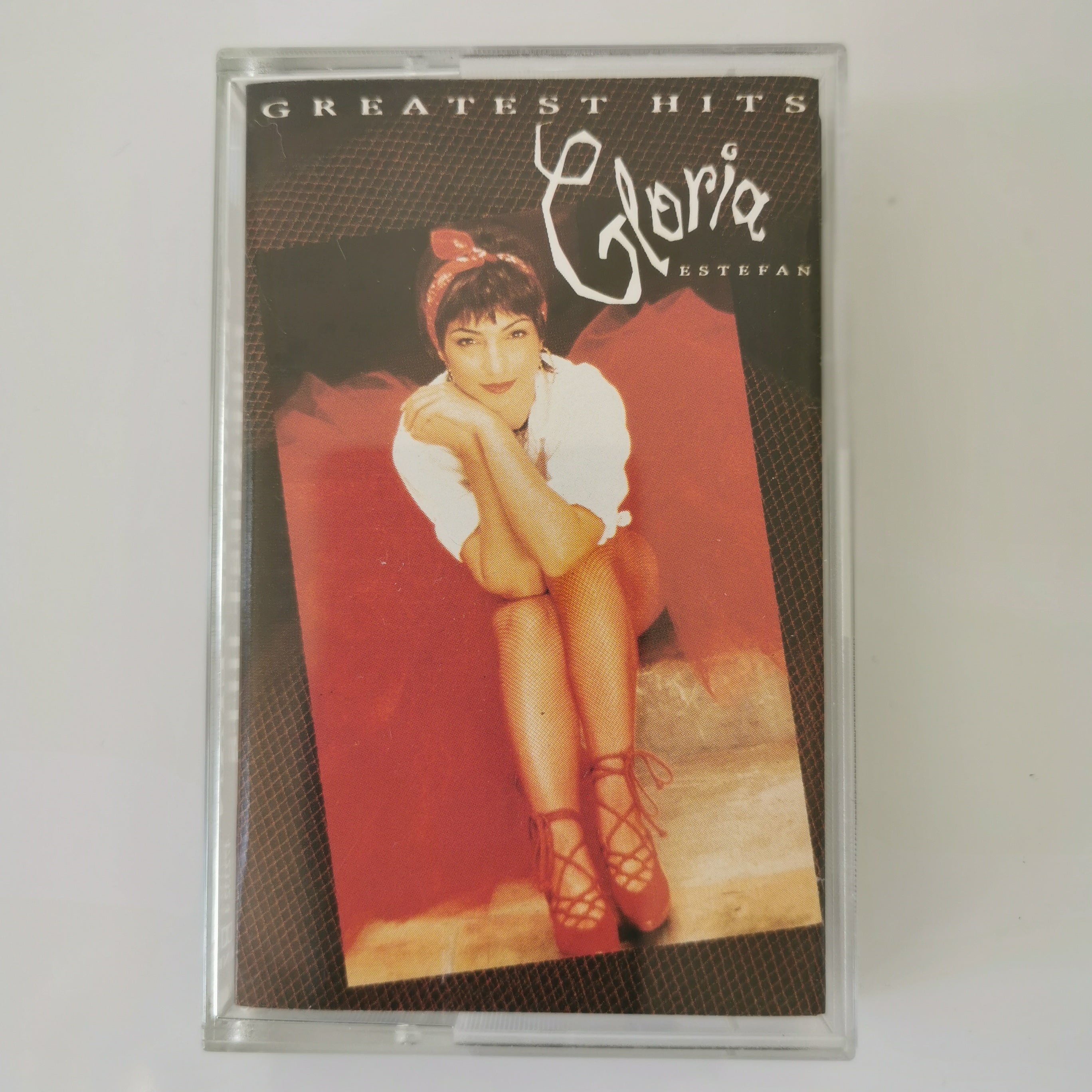 A cassette tape of Gloria Estefan's 'Greatest Hits' album in a clear plastic case, photographed against a plain light background.