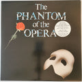 The Phantom of the Opera vinyl record cover, featuring a black background with the title in stylized blue and white lettering, a red rose on the left, and a cream-colored mask in the lower right corner.