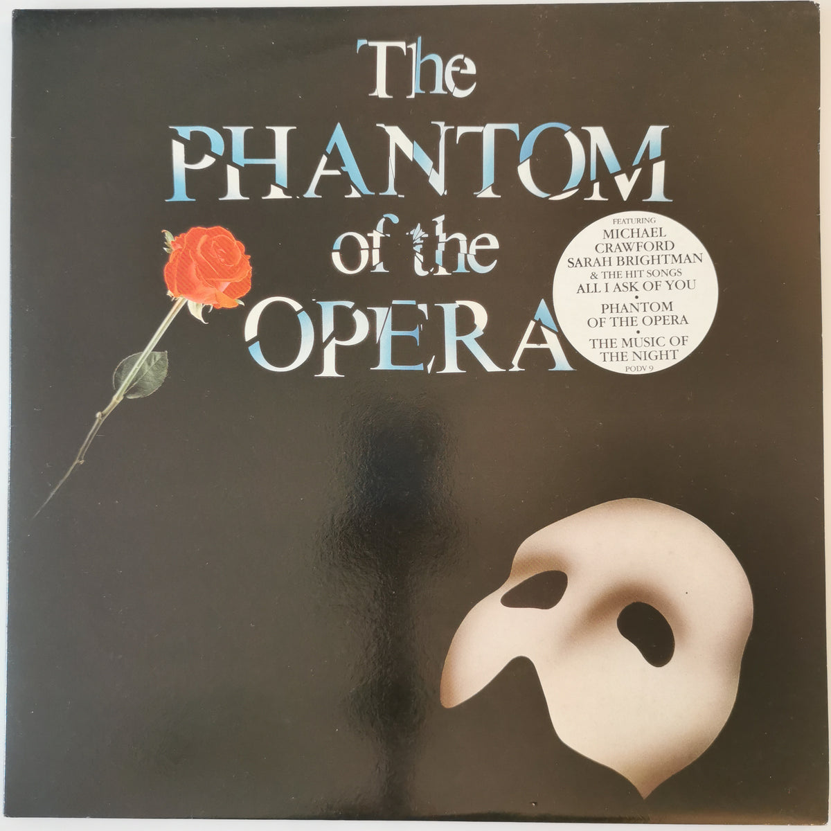 The Phantom of the Opera vinyl record cover, featuring a black background with the title in stylized blue and white lettering, a red rose on the left, and a cream-colored mask in the lower right corner.