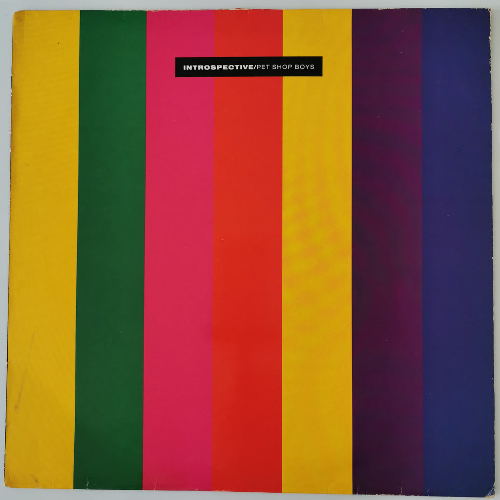 A square album or book cover featuring bold vertical stripes in yellow, green, pink, red, orange, purple, and blue, with a small black label near the top reading 'INTROSPECTIVE/FT SHOP BOYS'.
