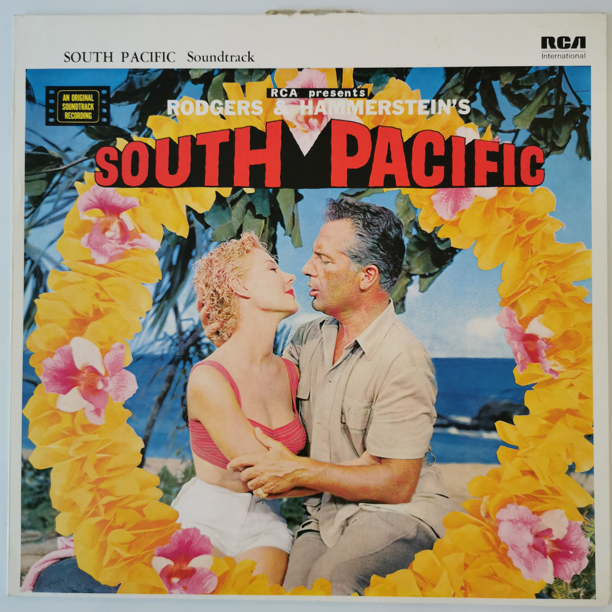 South Pacific soundtrack vinyl record cover by RCA, featuring a tropical beach scene with a couple embracing and a large yellow flower lei framing them. The title 'SOUTH PACIFIC' is printed in large red letters at the top, with RCA branding in the upper right corner.