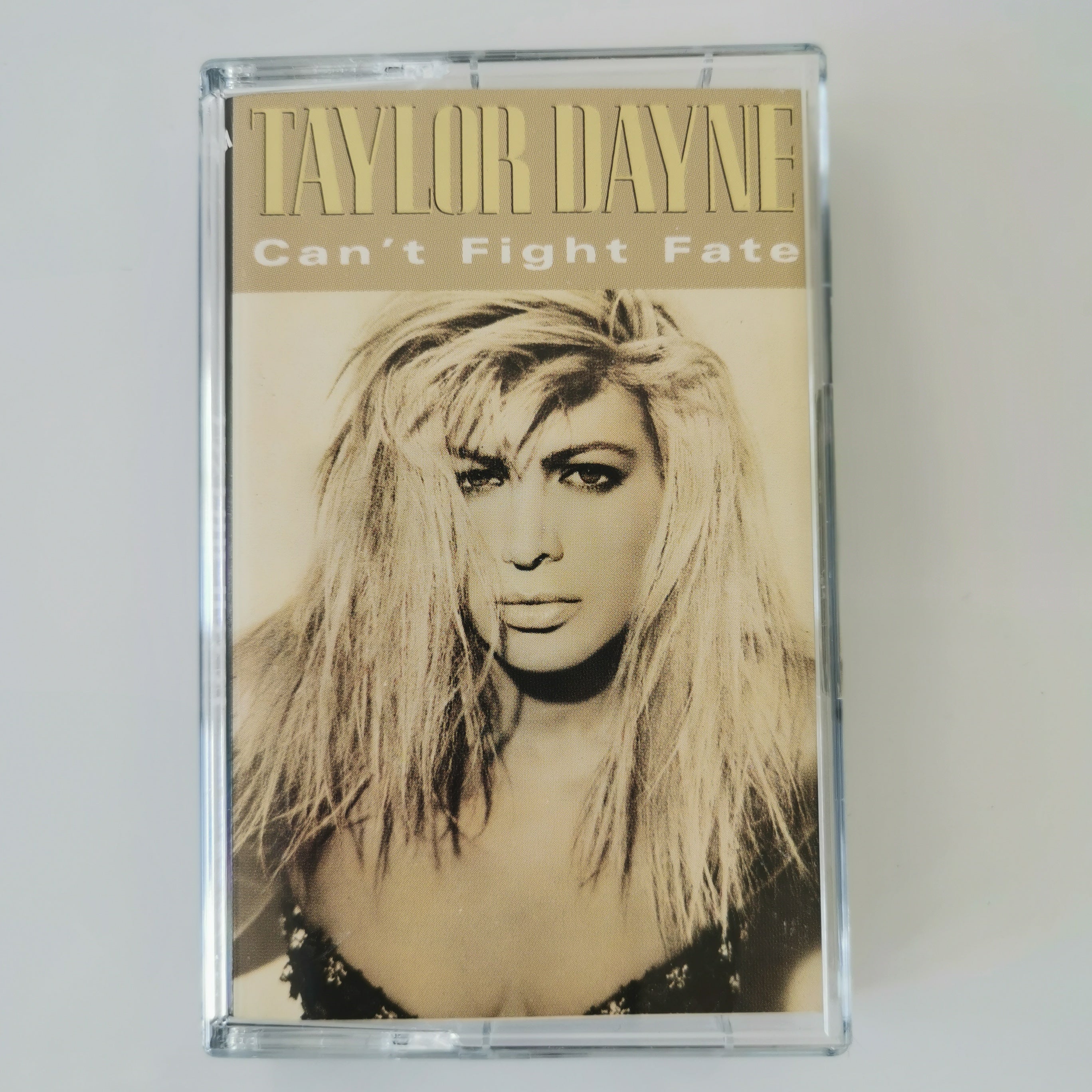 Taylor Dayne 'Can't Fight Fate' cassette tape in a clear plastic case, featuring a sepia-toned portrait of the artist with gold lettering.